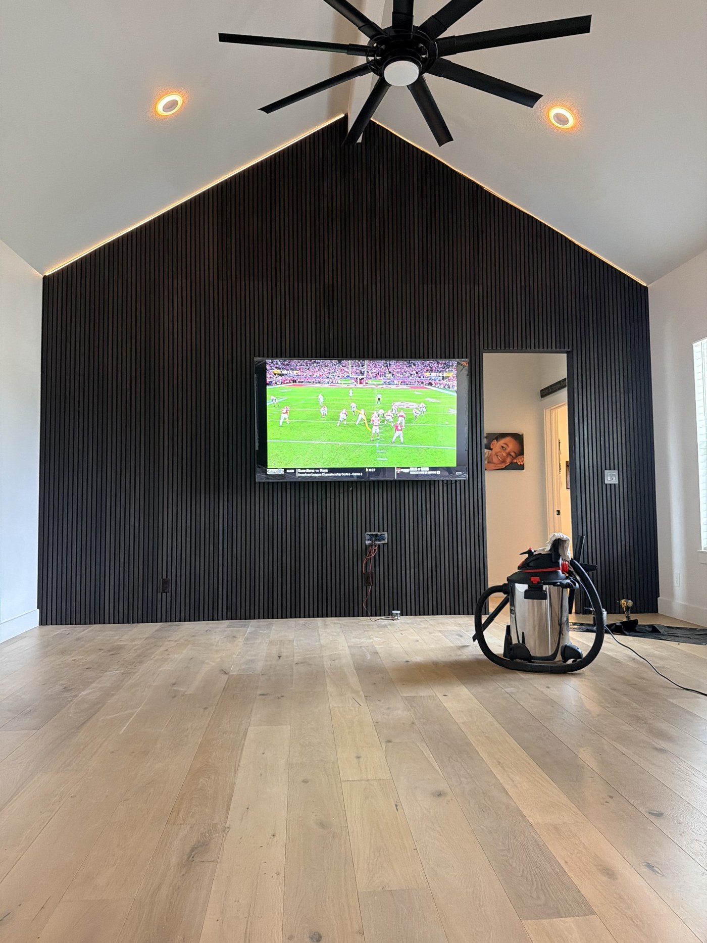 Black vertical slat accent wall with mounted TV and lighting along the vaulted ceiling